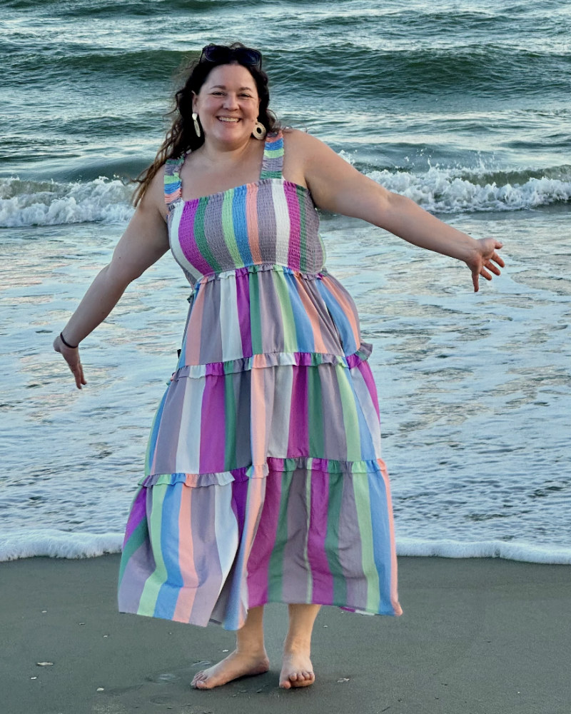 Jessica on the beach at sunset, arms out and smiling, the surf behind her.