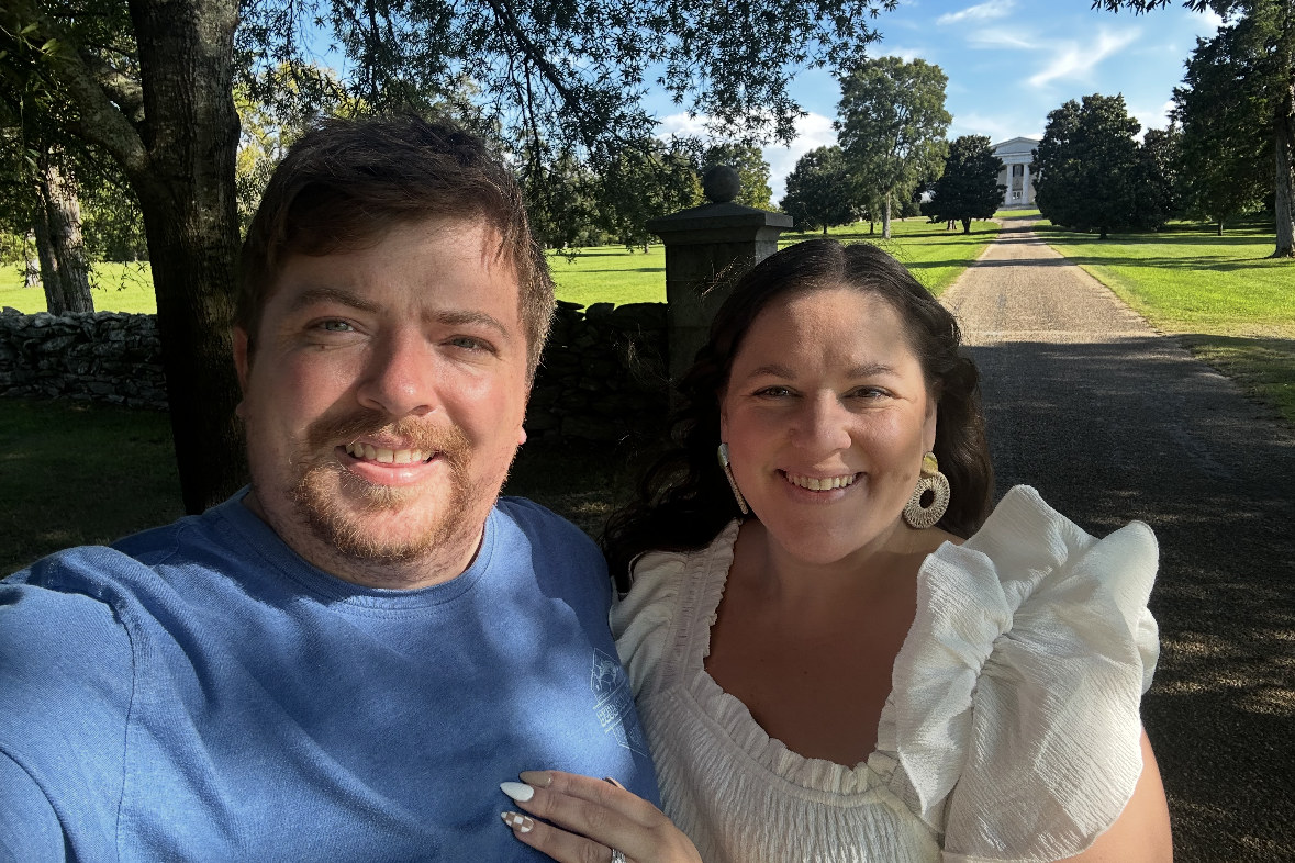 Kelly and Jessica together on a tree-lined drive, a white house at the far end of it.