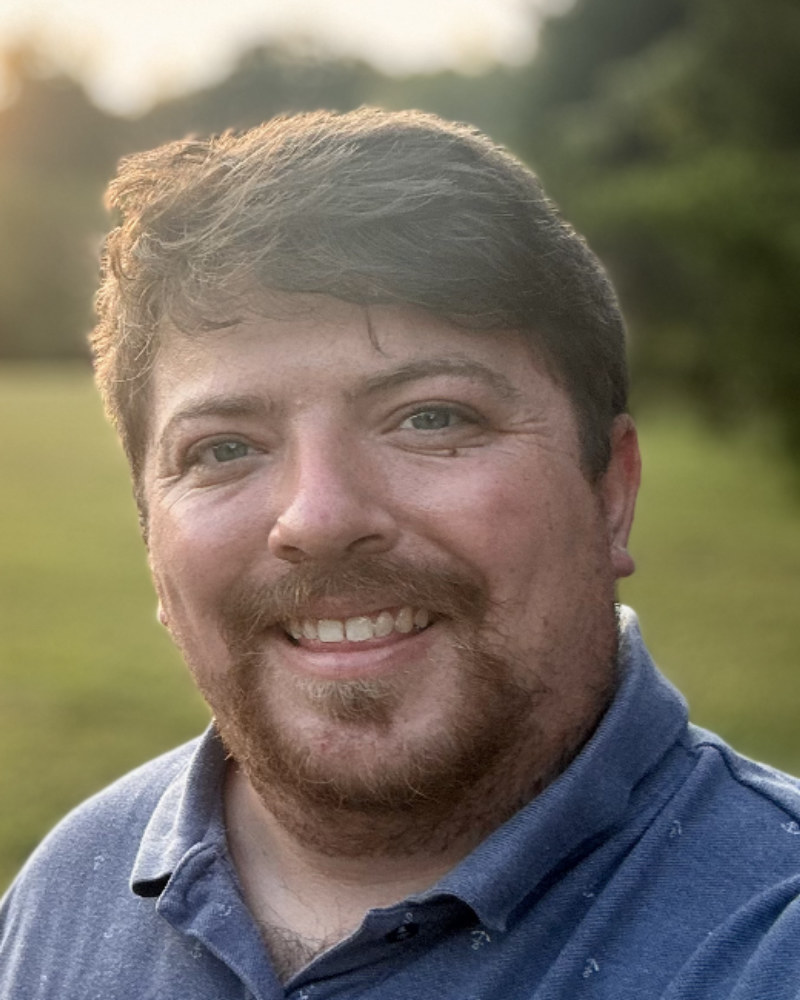 Kelly McDonald outdoors at sunset, smiling, in a blue collared shirt.